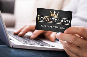 A hand holding a loyalty card while typing on a laptop