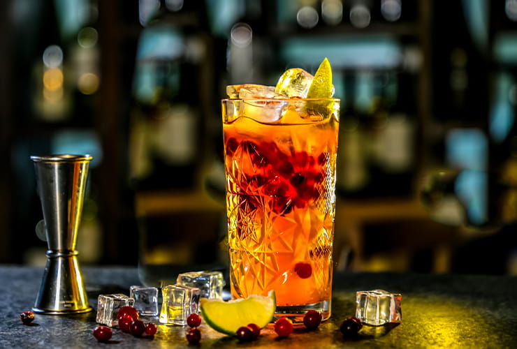 A tall glass with soft drink and a couple of ice cubes spilled on the counter